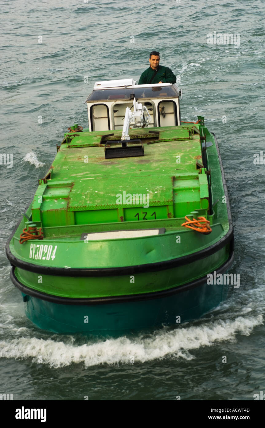 Editorial use only No model release Color vertical image of a green garbage boat piloted by an Italian trash man in Venice Italy Stock Photo