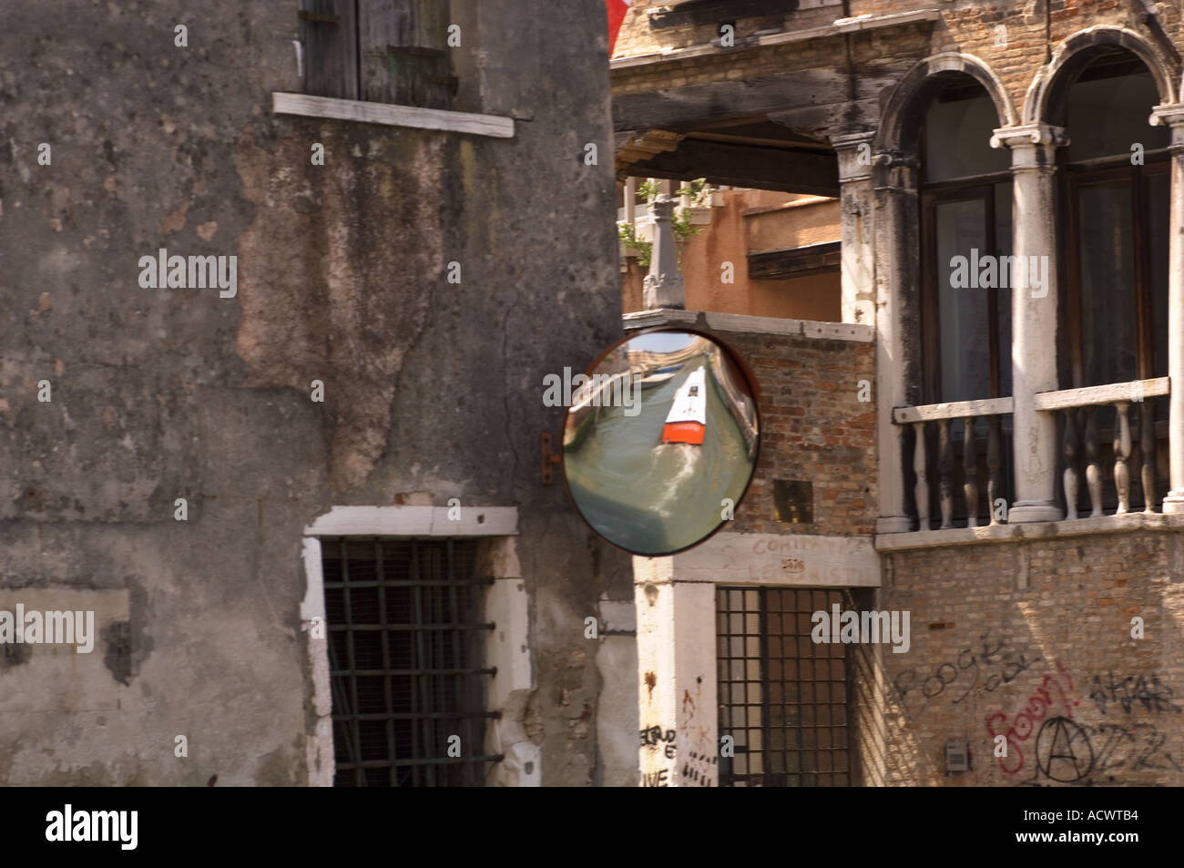 A traffic mirror posted at a canal interesection with a boat reflected in it in Venice Italy with graffiti on the buildings Stock Photo