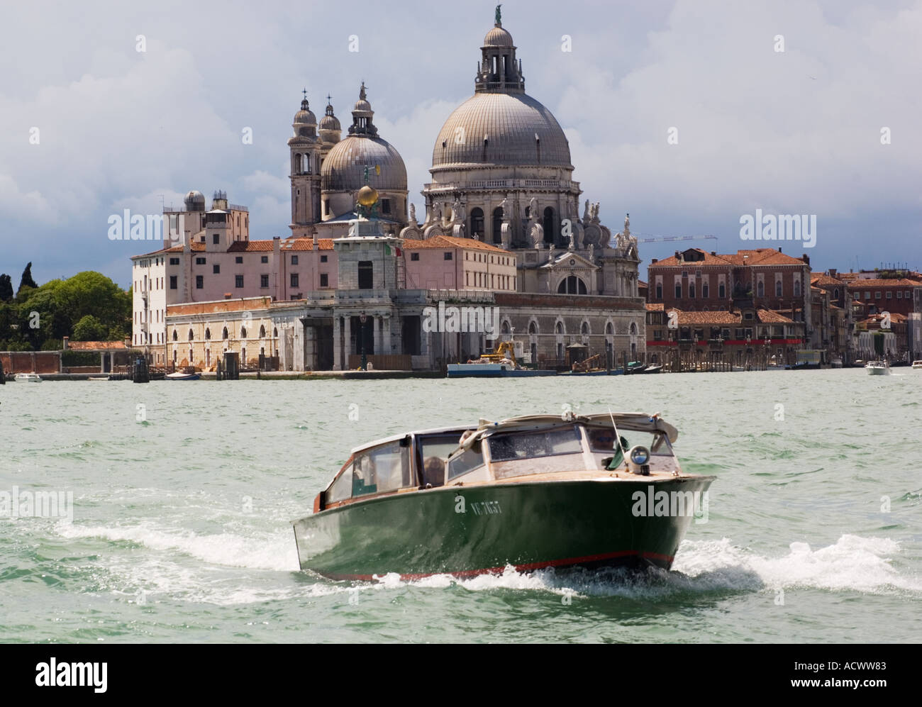 domes and spires of Chiesa Santa Maria della Salute and the banks of Venice from canal with green motor boat Stock Photo