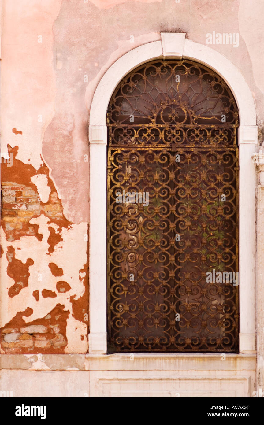 Color vertical image of a doorway covered with a rusted iron grate in a pink stucco covered brick building in Venice Italy Stock Photo