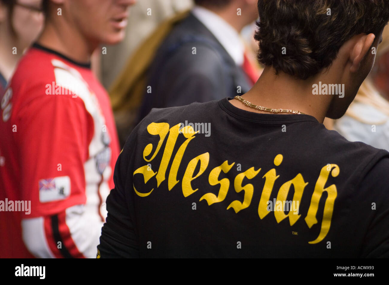 Color horizontal image of a young man from the back wearing a t shirt emblazzoned with the word Messiah in a crowd of people Stock Photo