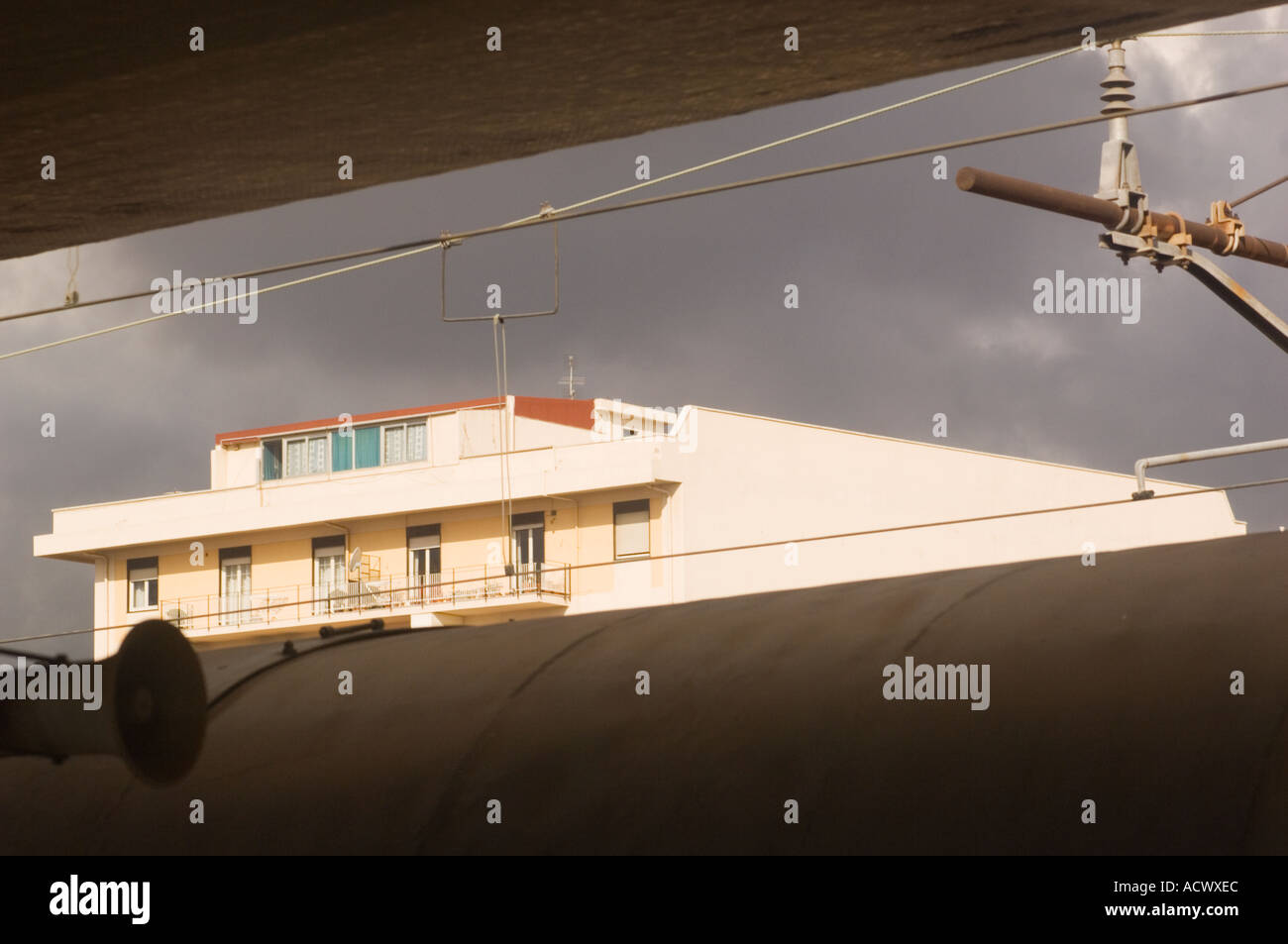 sunlit apartment building in Messina Sicily from train station over top of train roof and below ceiling of the train platform Stock Photo