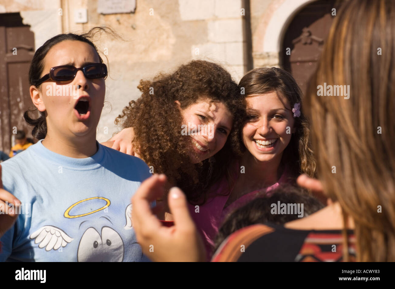 Editorial use only No model release teenage girls singing and clapping in April 9 Plaza in Taormina Italy with town library Stock Photo