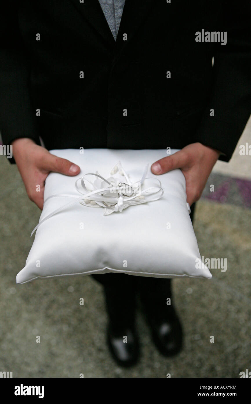 A Ring Bearer Holding Up A White Pillow With The Wedding Rings