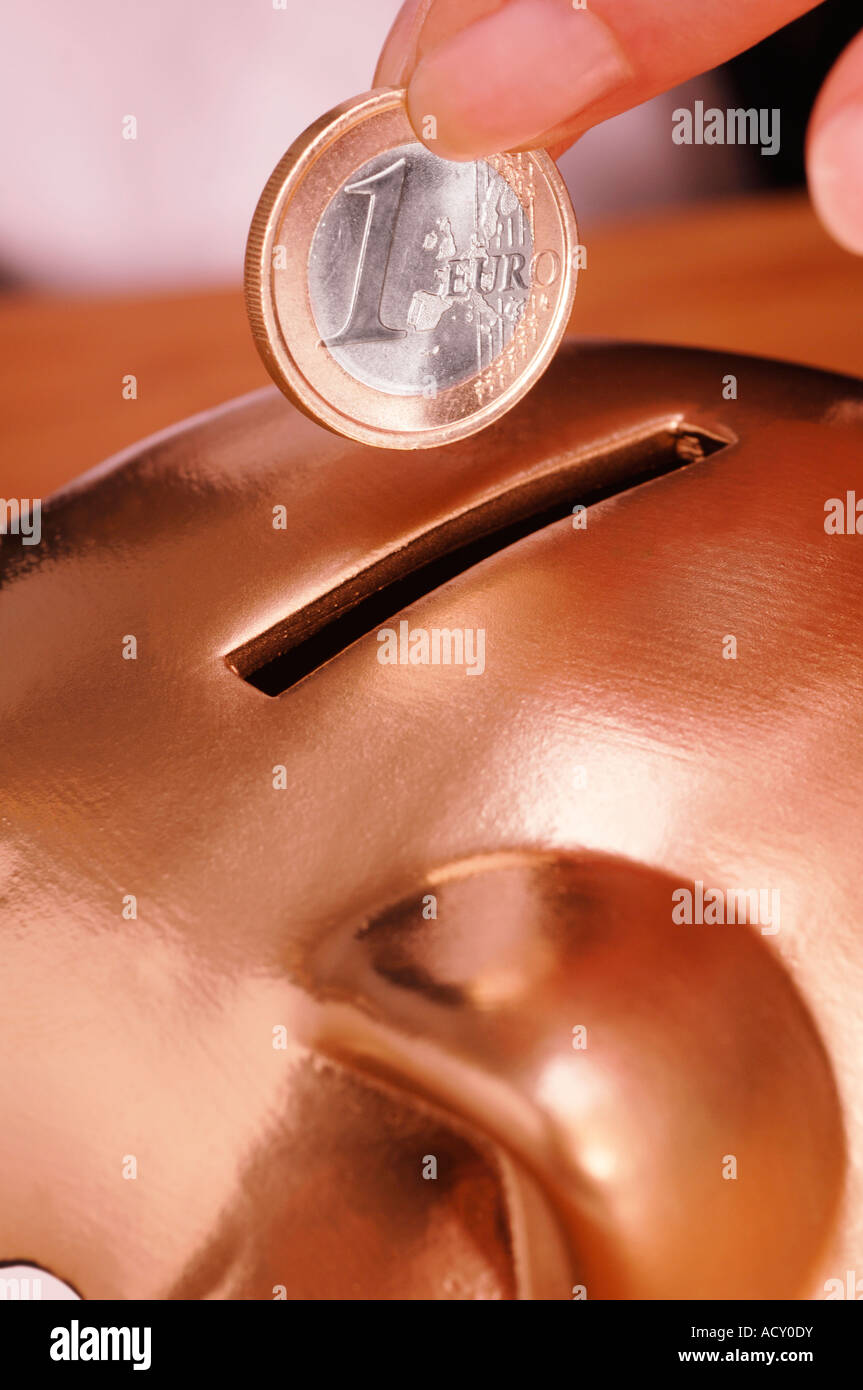 Woman putting euro coin into golden piggy bank Stock Photo - Alamy