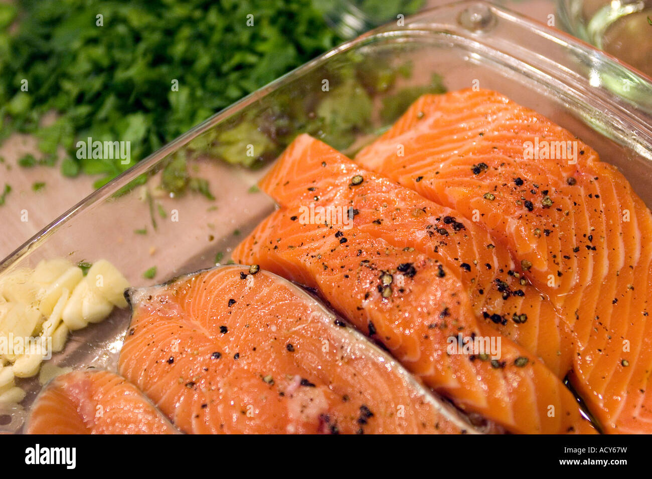 slices of salmon sit in a pyrex dish before being  cooked. on the side are seen some sllices of garlic  and some parsley Stock Photo