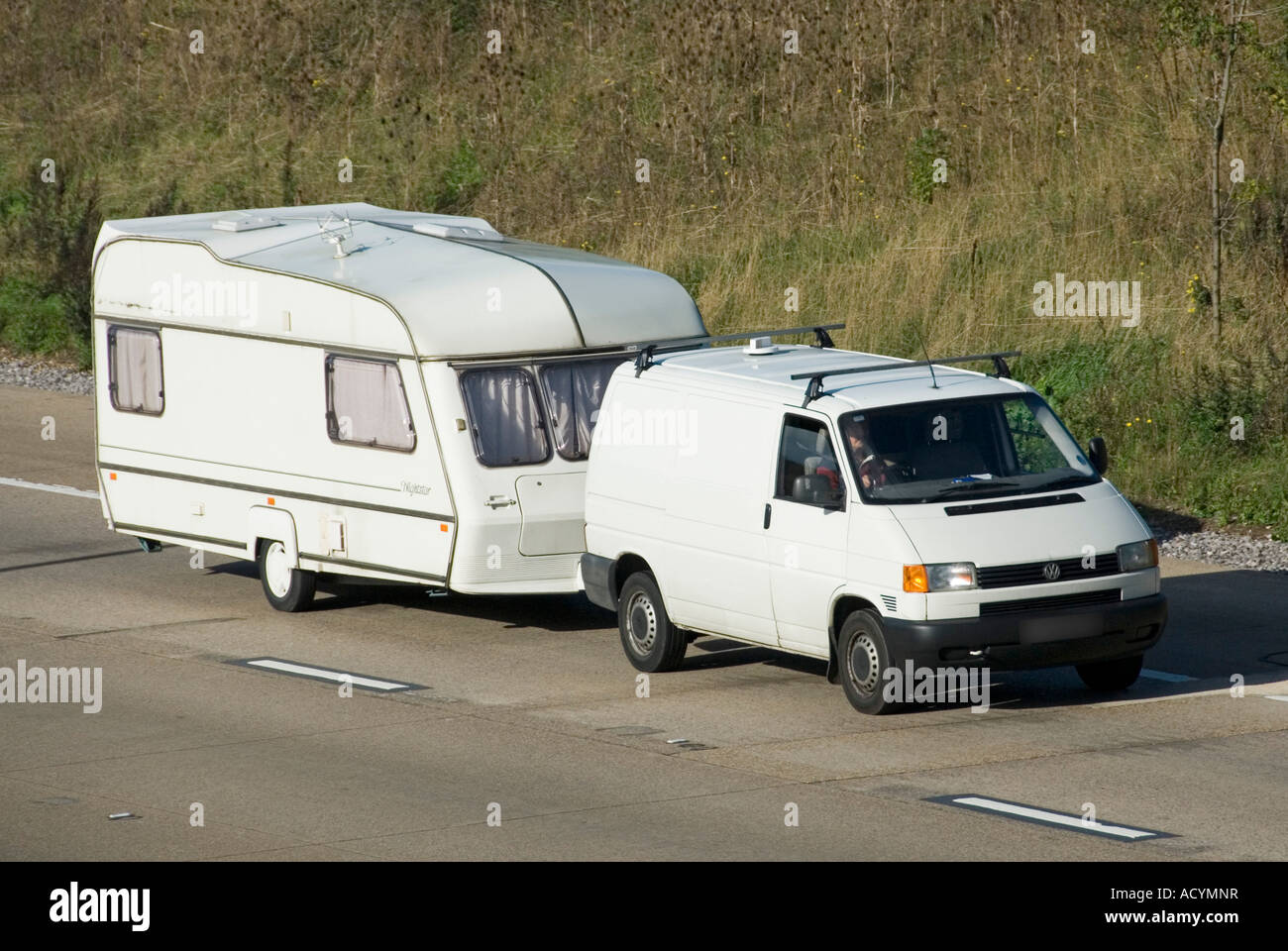 M25 motorway white van towing white caravan both clean unmarked with obscured number plate Stock Photo