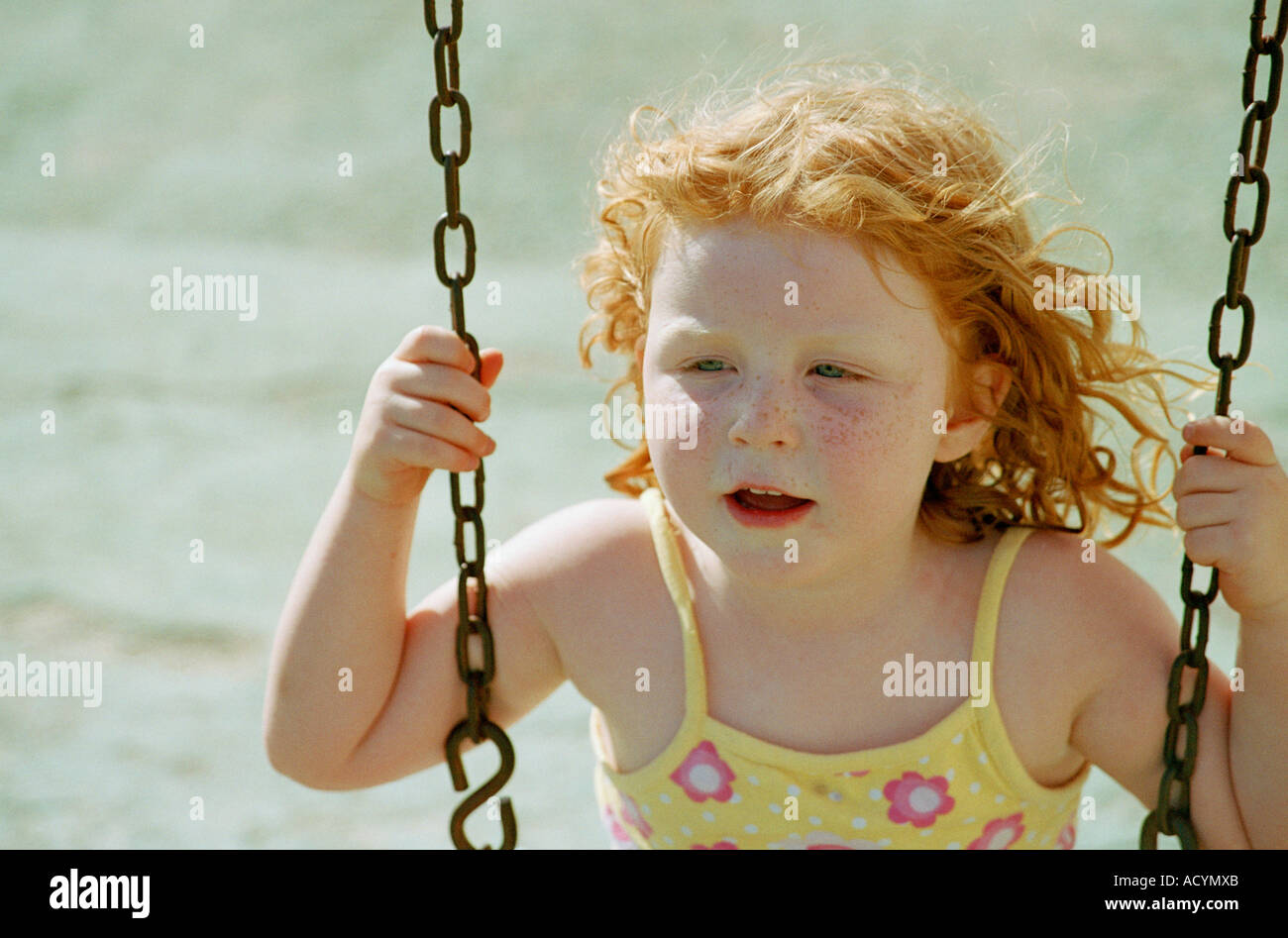 a small girl playing on a swing with red hair blowing in the wind ...
