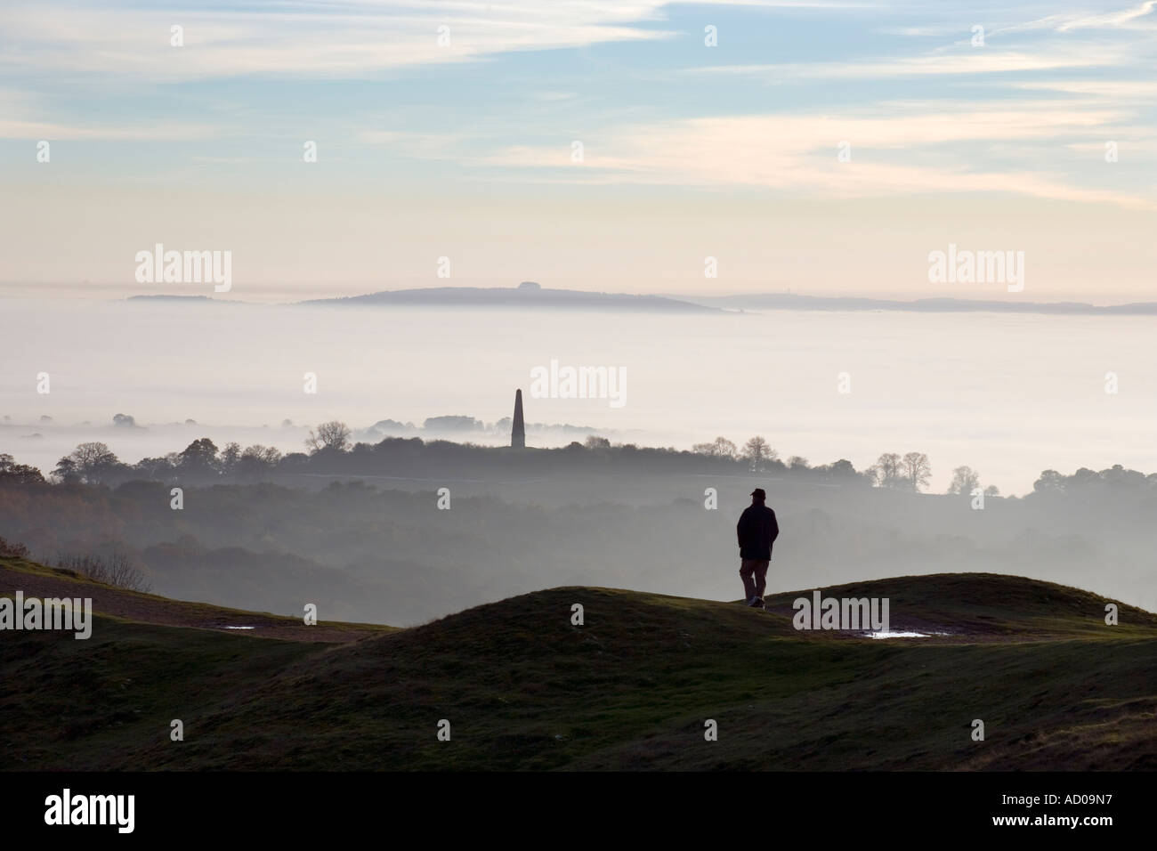 A walker on top of the Malvern Hills in Worcestershire UK above dense fog covering surrounding countryside Stock Photo