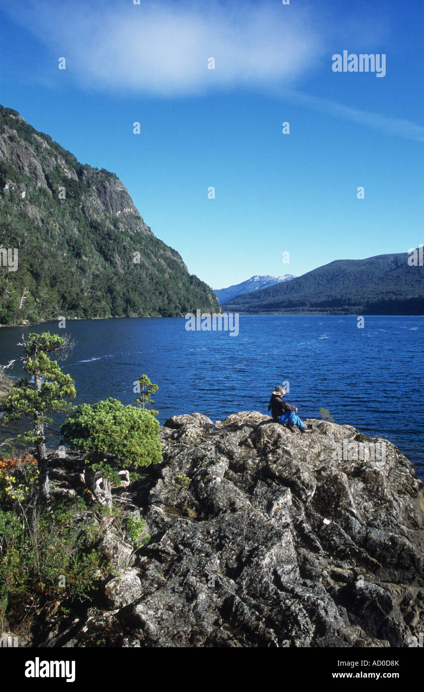 Trekker sitting on rocks looking at view on shore of Lake Paimun looking at view, Lanin National Park, Argentina Stock Photo