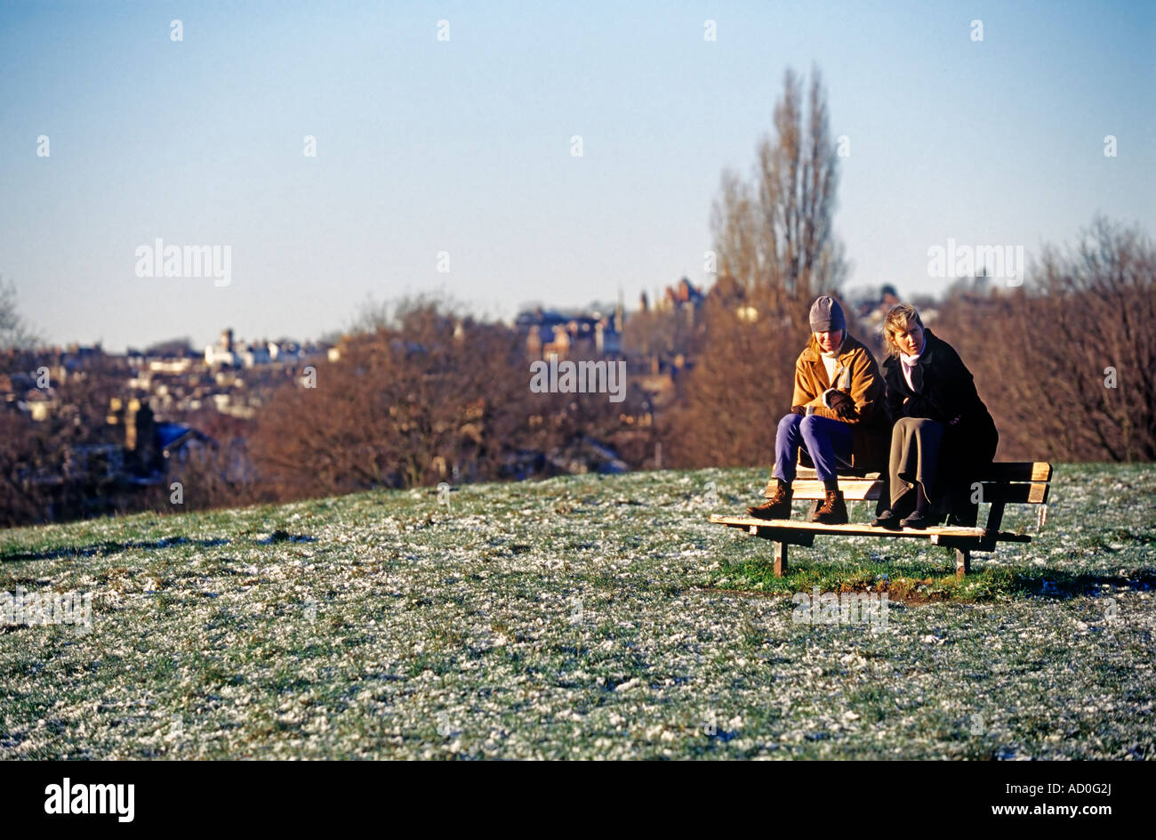 Two women sitting together on frosted bench in winter, Hampstead Heath, London, UK Stock Photo
