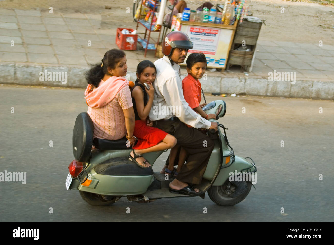 Horizontal aerial view of an entire Indian family on one tiny moped travelling along the road at speed in central Delhi. Stock Photo