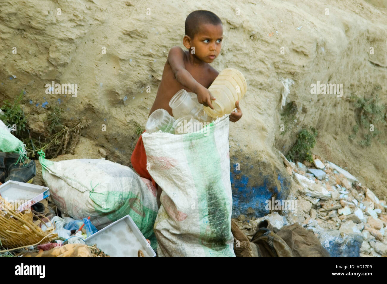 Horizontal portrait of a poor young boy collecting plastic containers on a pile of rubbish for recycling. Stock Photo