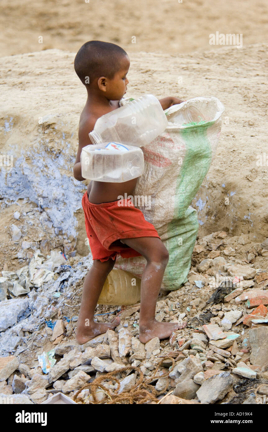 A poor young boy collects plastic containers from alongside the Ganges river trying to earn some money. Stock Photo