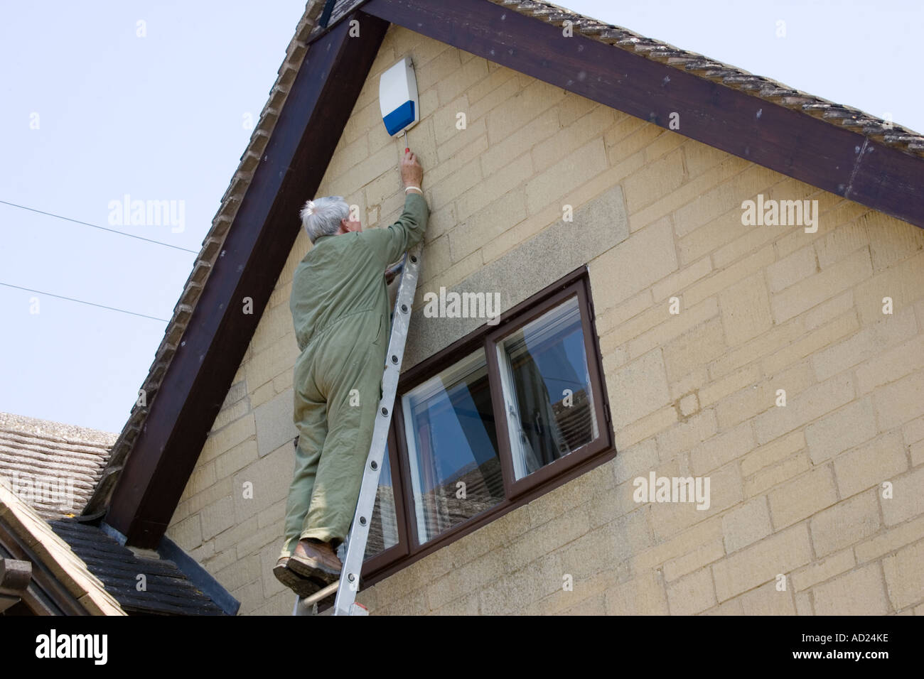 Electrical engineer checking burglar alarm unit high on wall of house