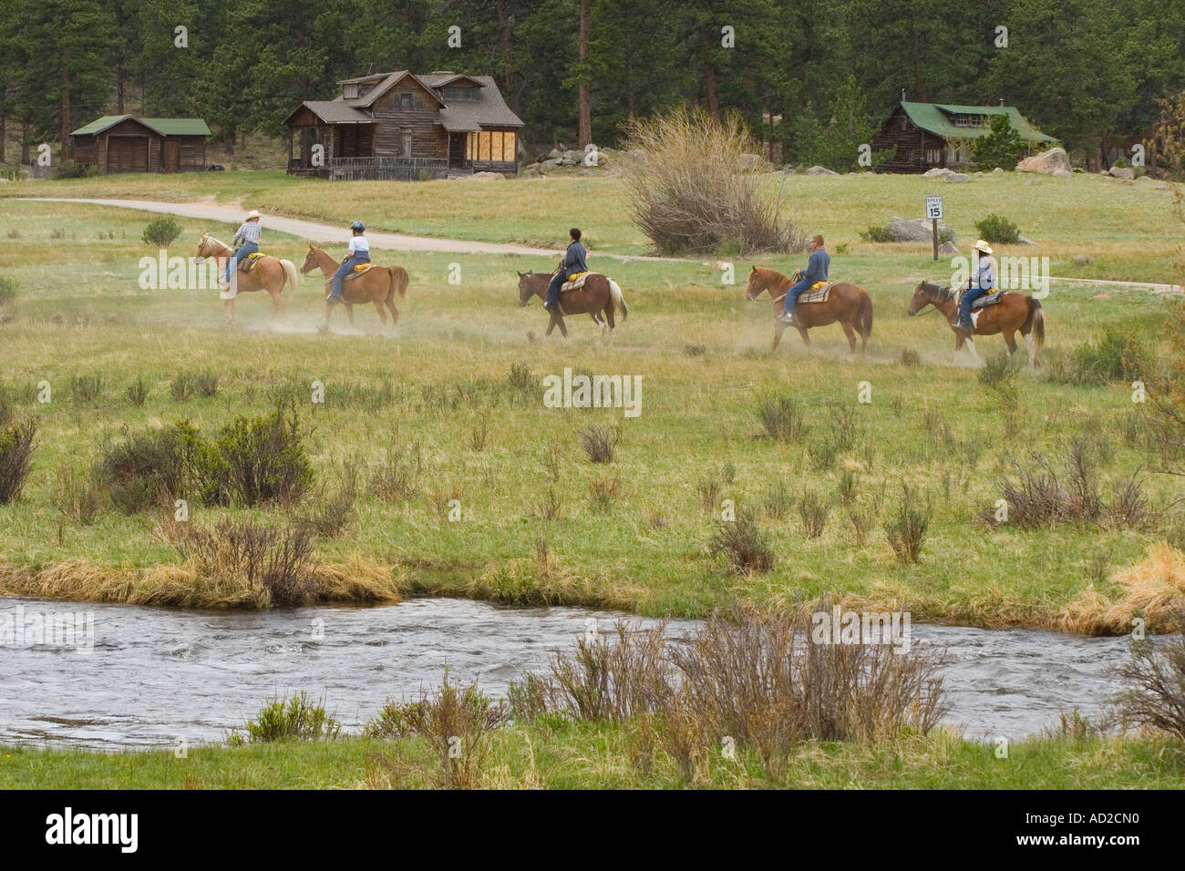 Five Riders On Trail Ride In Front Of Log Cabins Mountain Stream