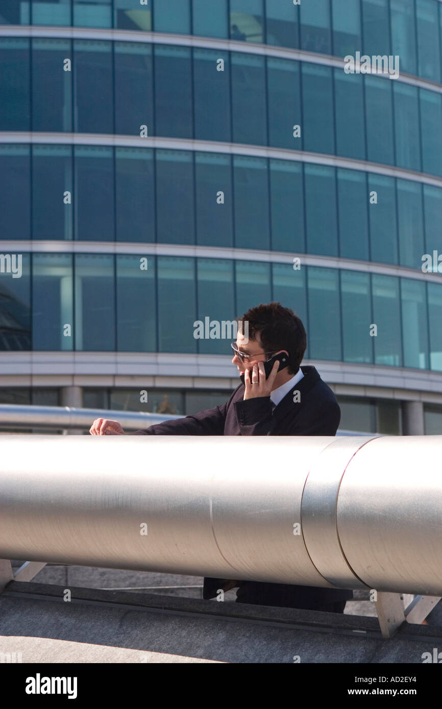 Young businessman rests on railing while talking on mobile phone in More London Place development near City Hall London Stock Photo