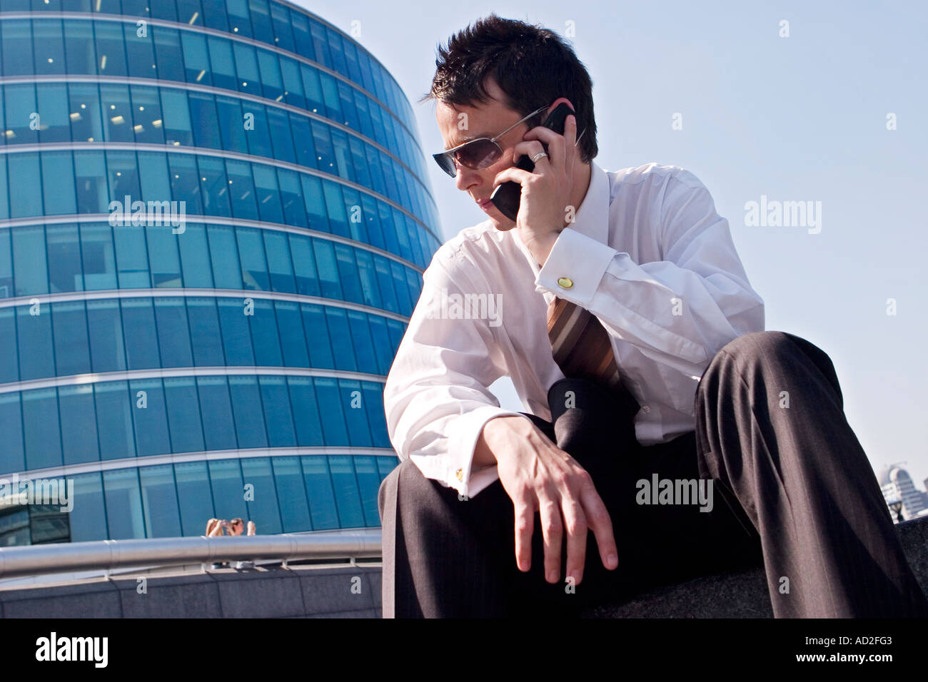 Young businessman sits down whilst using mobile phone More London Place development near City Hall London Stock Photo