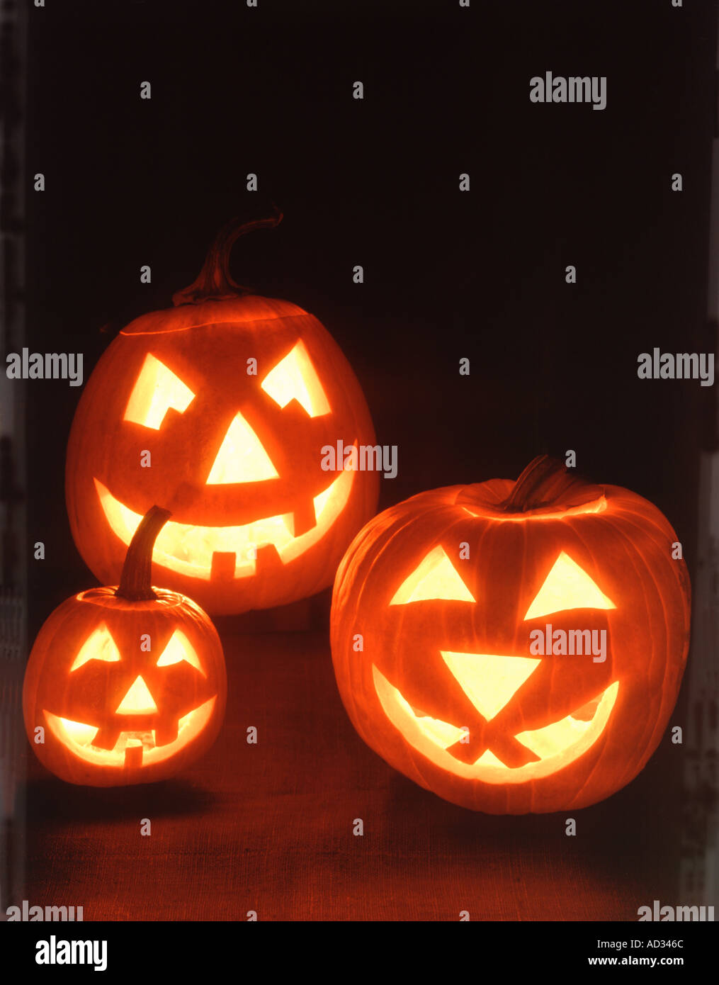 Three lighted Halloween Jack O Lanterns with smiling carved faces on a ...