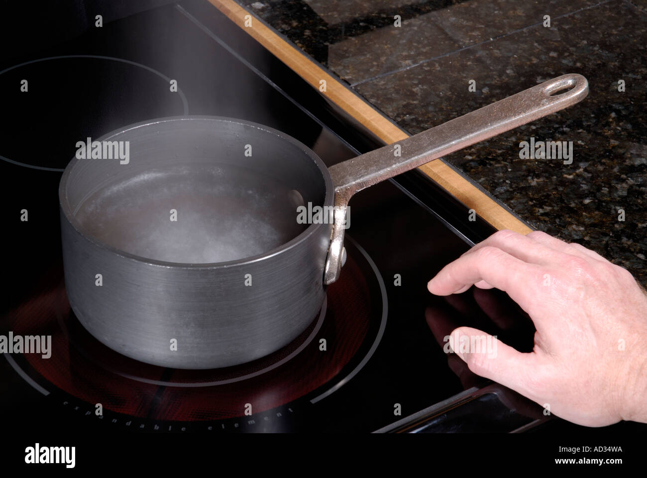 Pot with boiling water on burner with hand on stove top showing stove