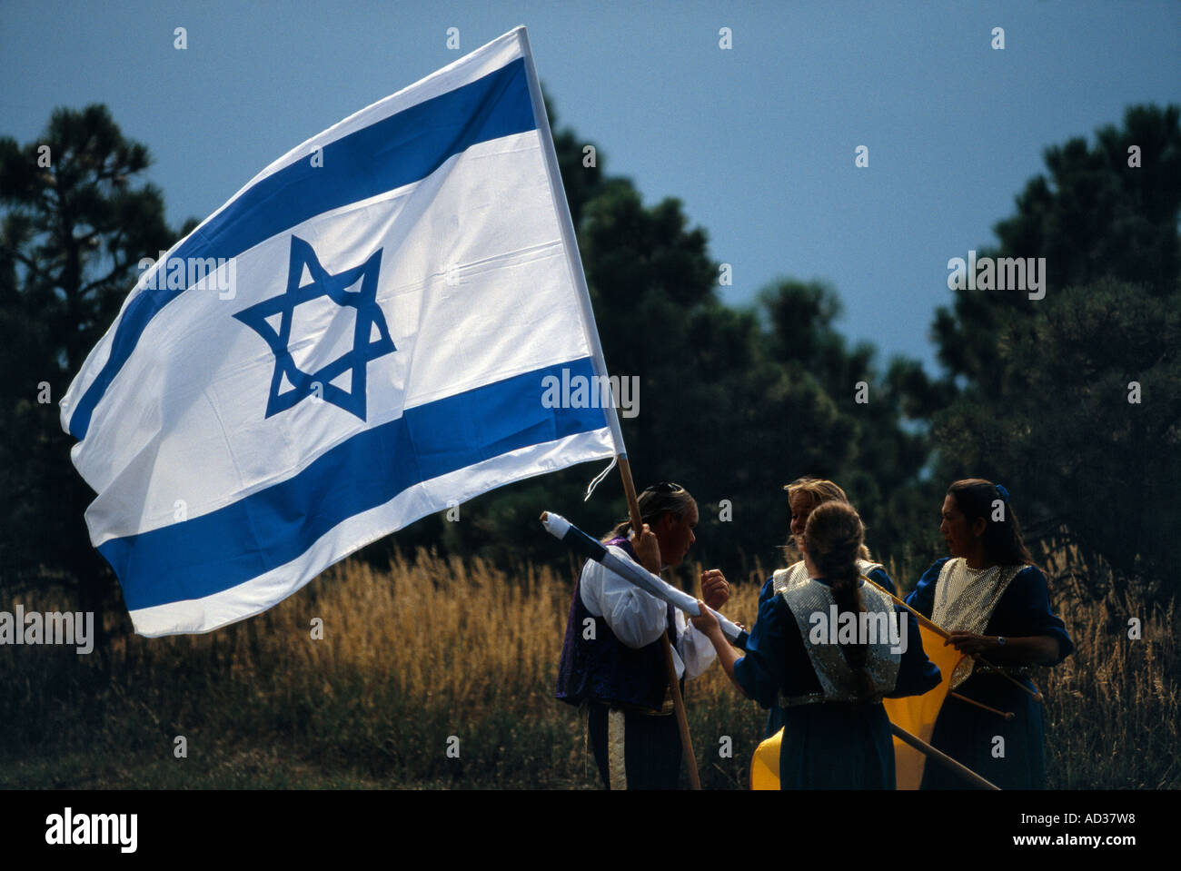 Group wearing costumes carries the flag of Israel in a mountain field. Stock Photo
