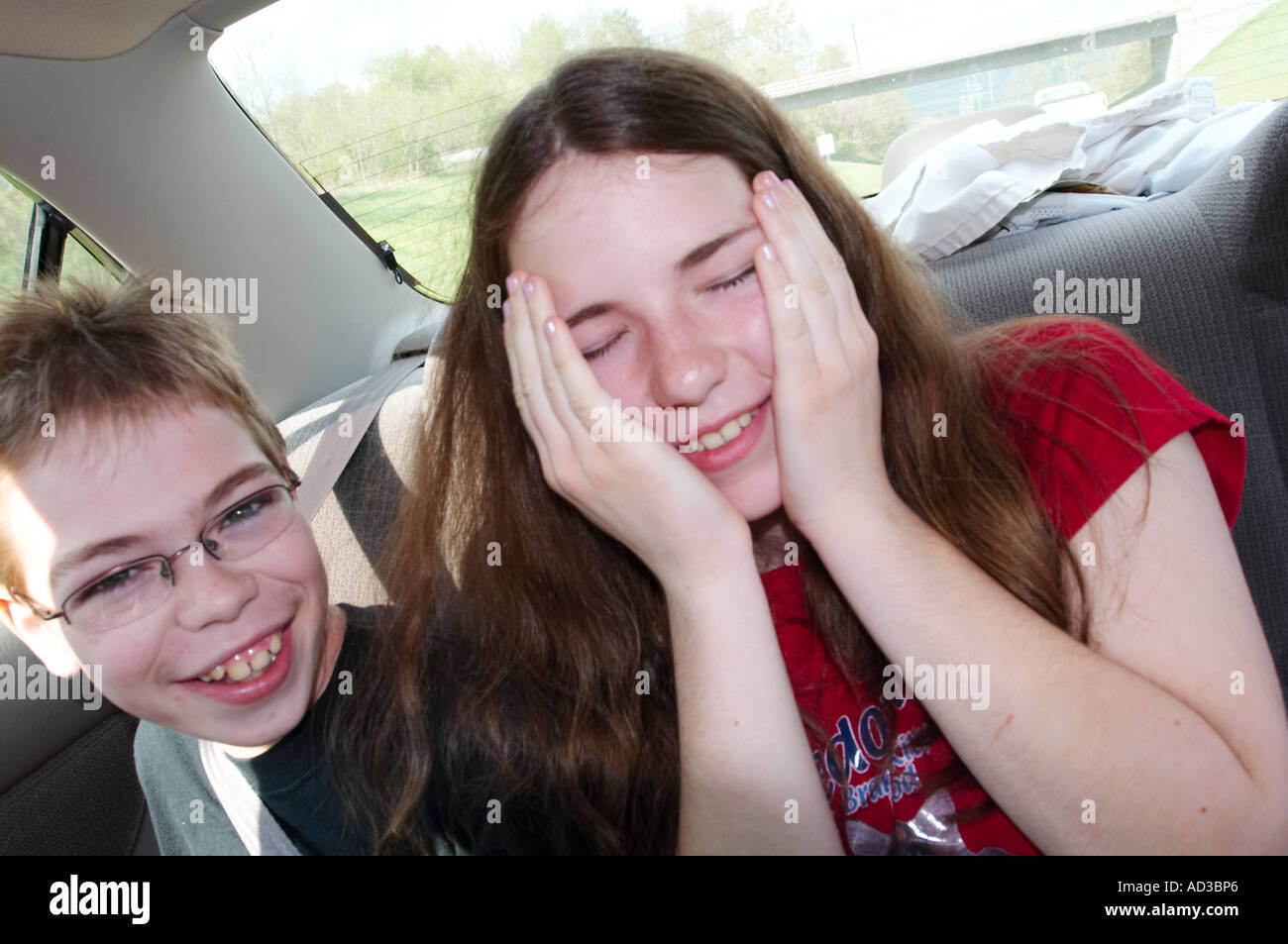 A brother and sister making funny faces in the back seat of a car