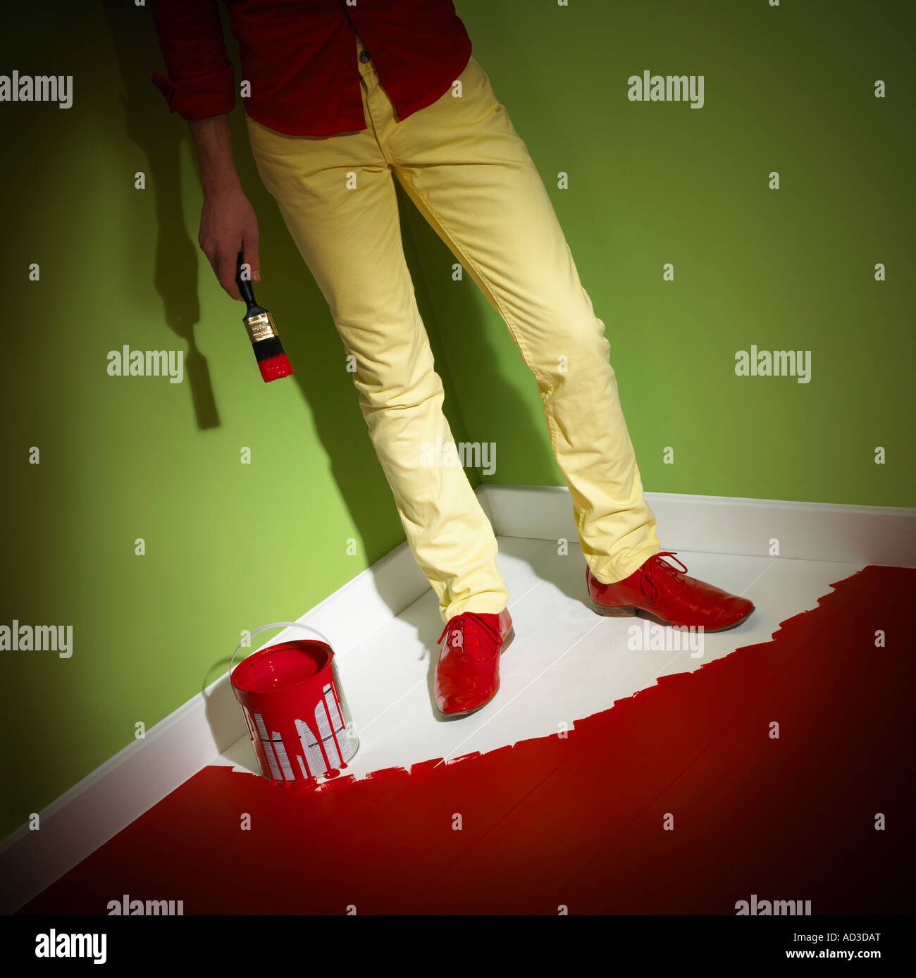 YOUNG MAN WEARING YELLOW JEANS TRAPPED IN CORNER OF ROOM BY WET PAINT ON FLOOR Stock Photo