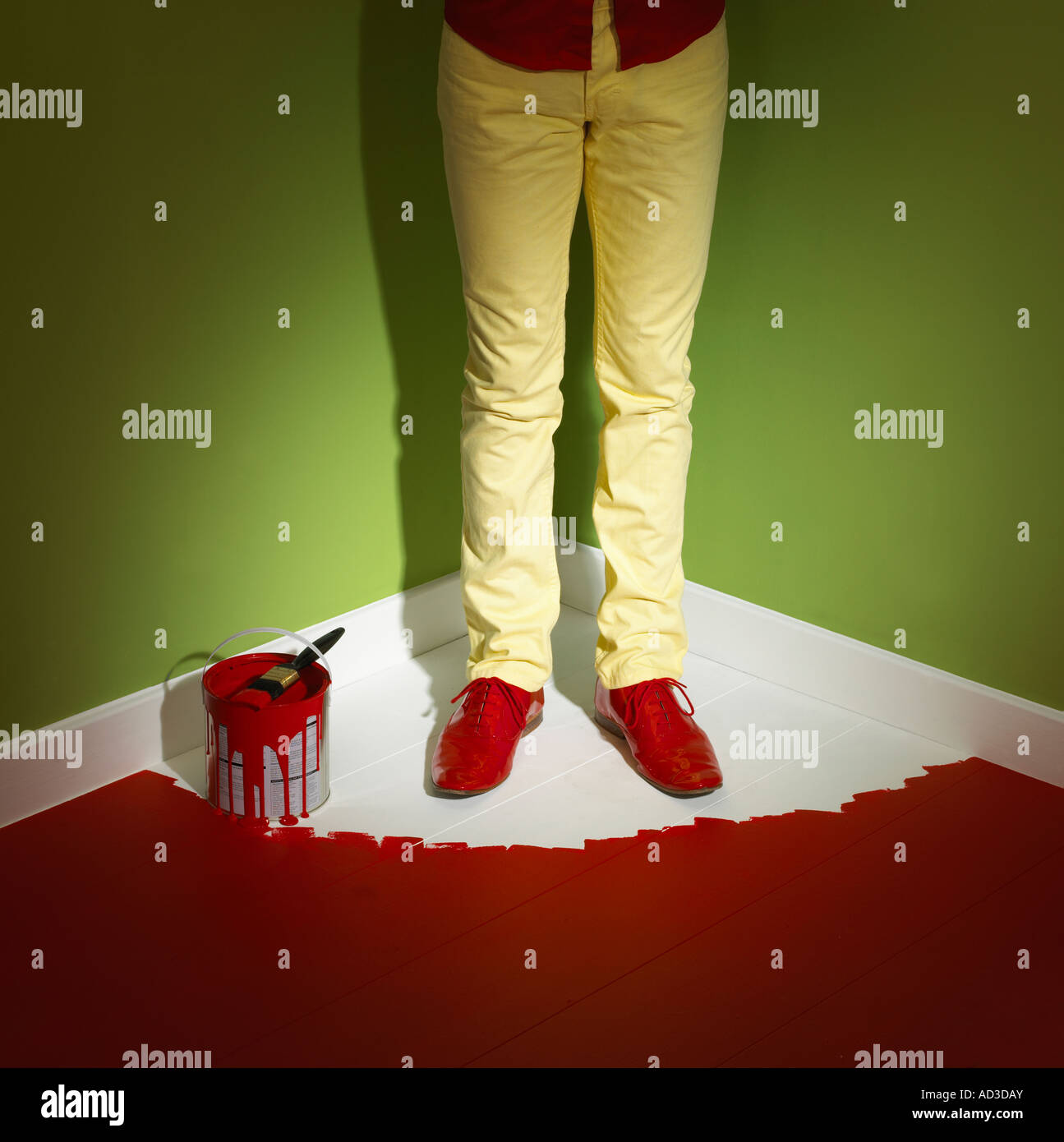 YOUNG MAN WEARING YELLOW JEANS TRAPPED IN CORNER OF ROOM BY WET PAINT ON FLOOR Stock Photo