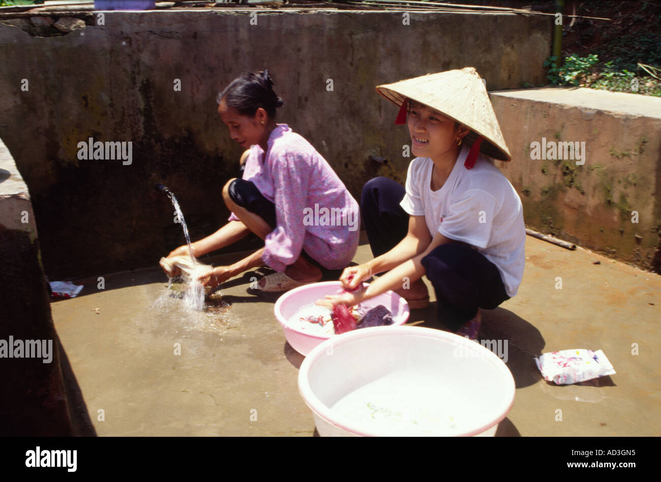 Women wearing straw hats do washing at communal water well in Mai Chau