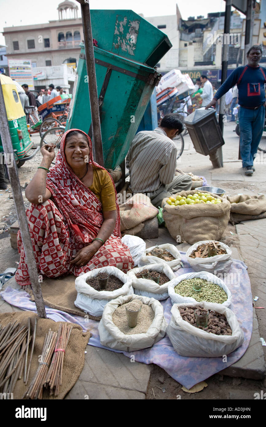 An Indian woman selling rice and grain on the pavement of a busy street ...
