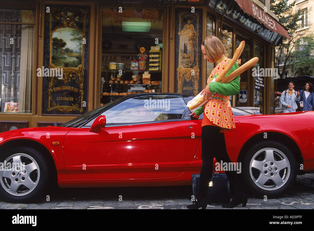 French woman entering sports car with baguettes outside bakery or boulangerie in Paris Stock Photo