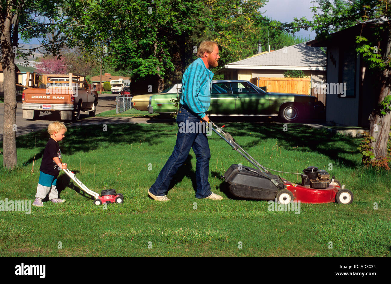 Son imitates his father while mowing the lawn  Stock Photo