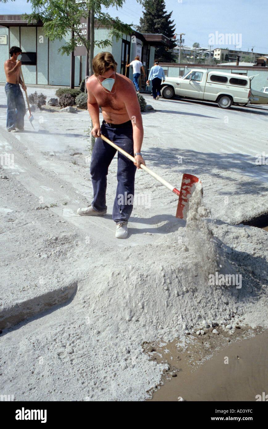 People wearing face masks clean up ash in the aftermath of the Mount St