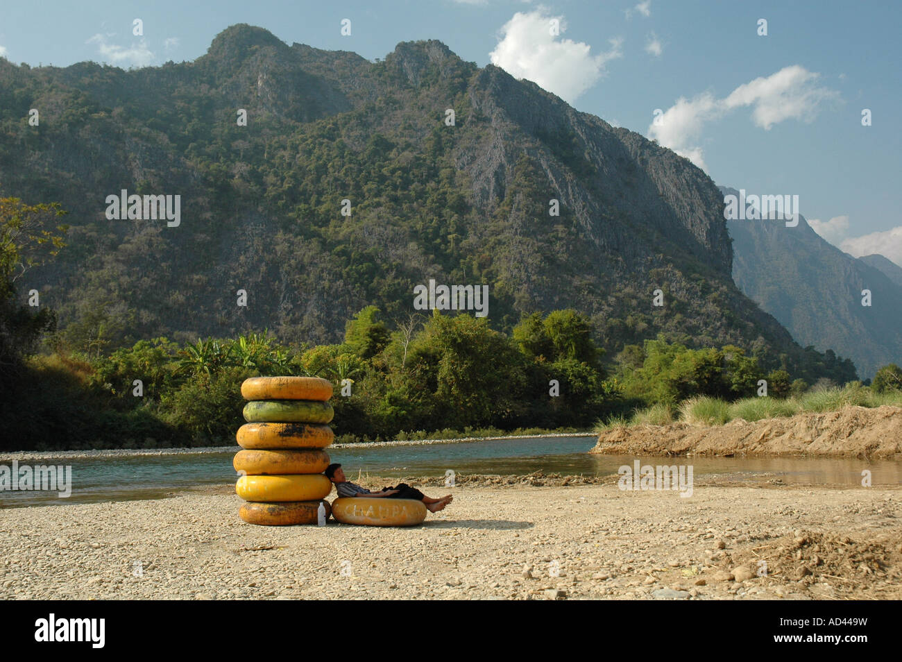 A young boy lays in the shade of inflated inner tubes which he hopes to rent to tourists to float down the river in Laos. Stock Photo
