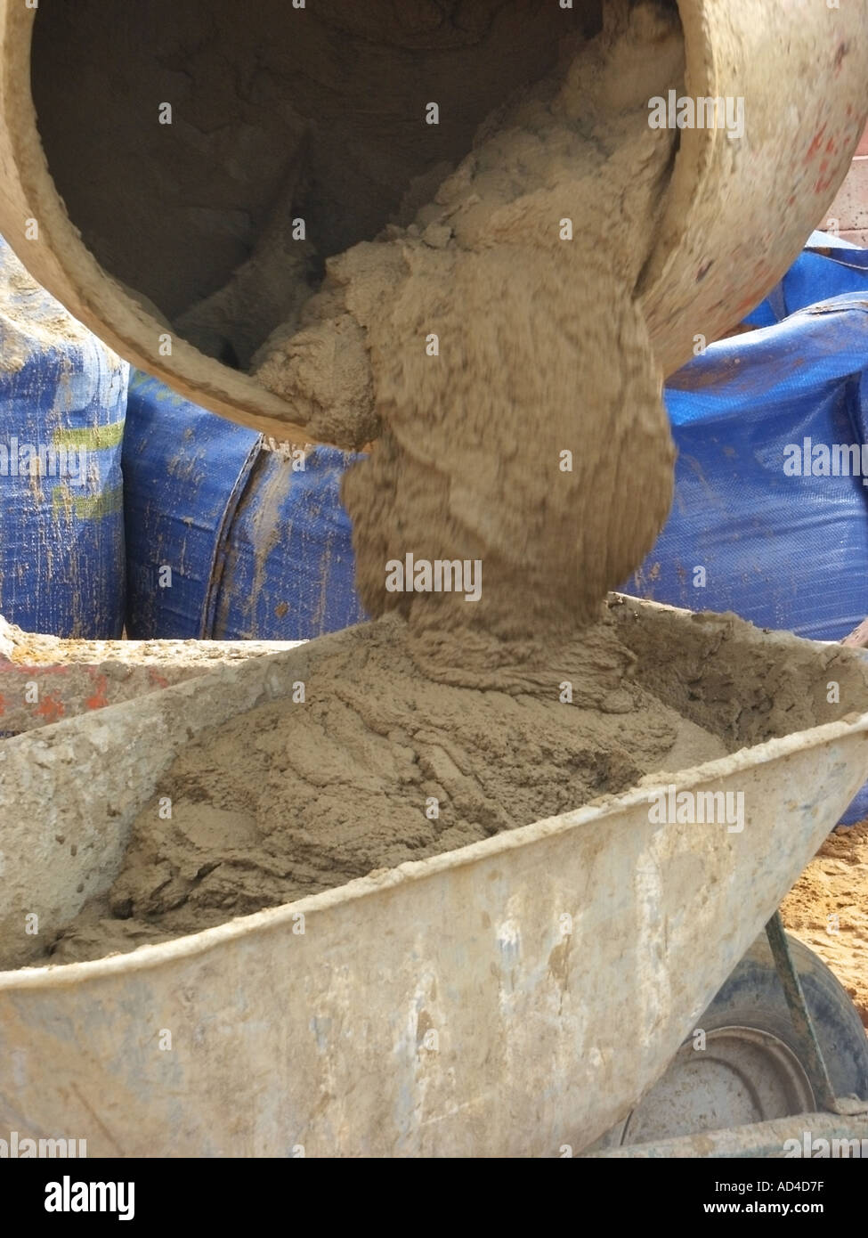 House building site close up of diesel powered cement mixer discharging bricklaying mortar into wheelbarrow Stock Photo