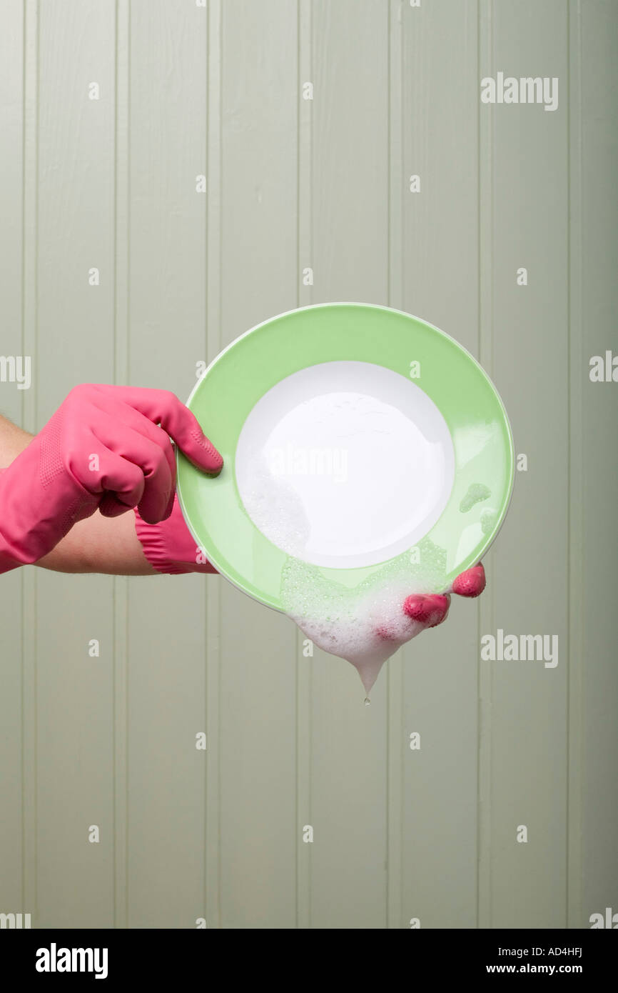 Detail of a person wearing rubber gloves and holding a clean plate Stock Photo