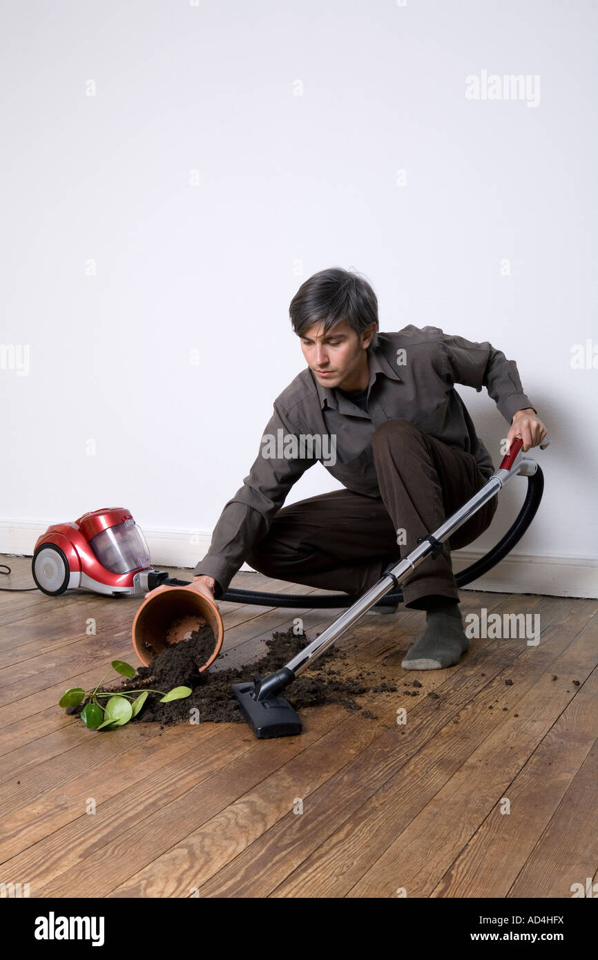 A man vacuuming up soil from a spilt potted plant Stock Photo