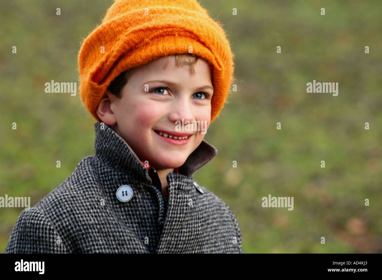 portrait of young boy smiling and wearing orange woollen hat and winter coat, outside on a winter's day Stock Photo