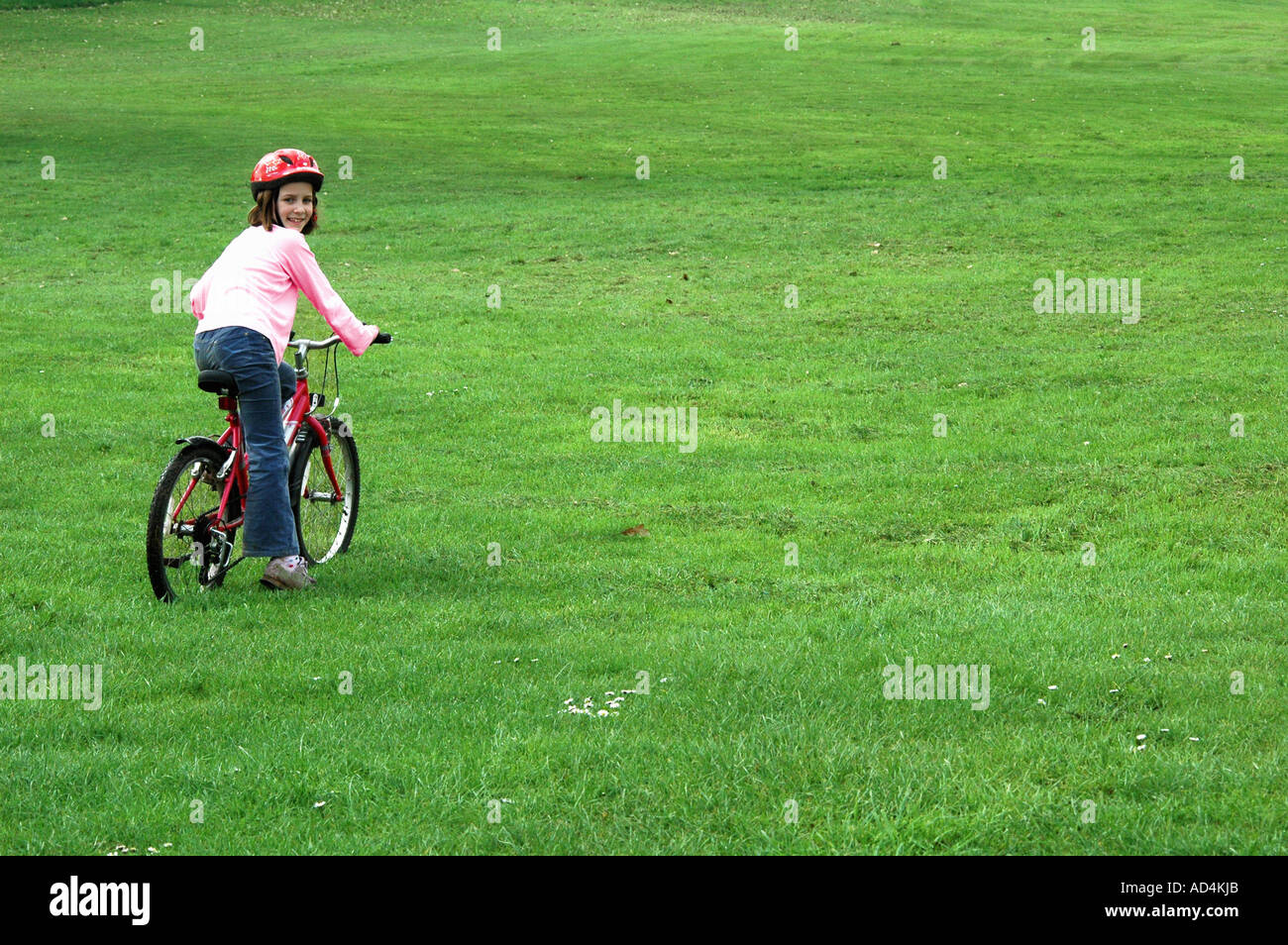 child wearing safety helmet and riding a bike over the grass in the park Stock Photo