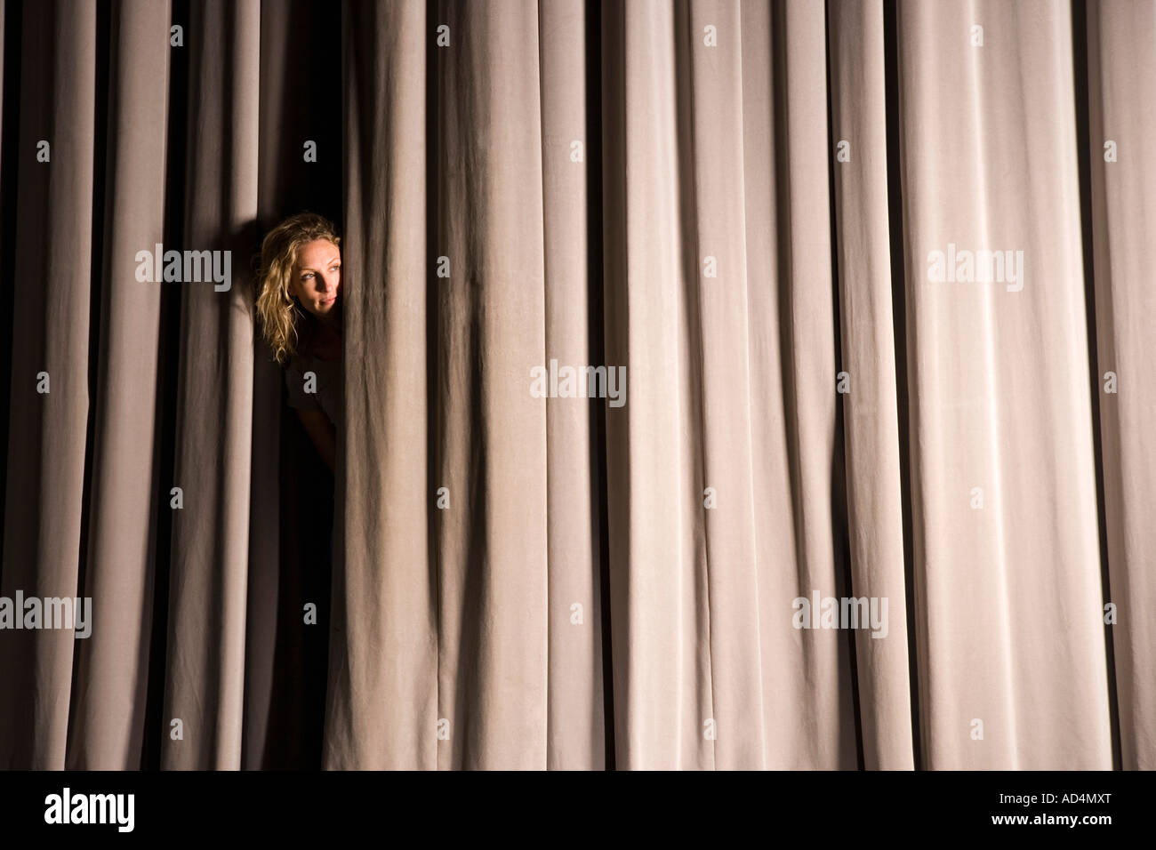 A woman peeking through a stage curtain Stock Photo