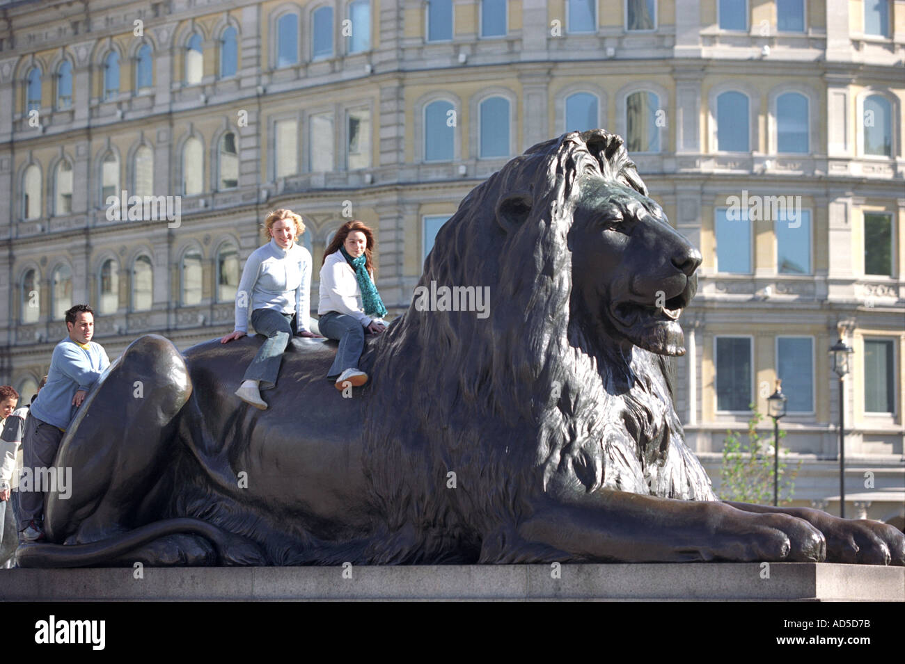 Tourists sit on the back of a lion statue in Trafalgar Square, London, Britain, UK Stock Photo
