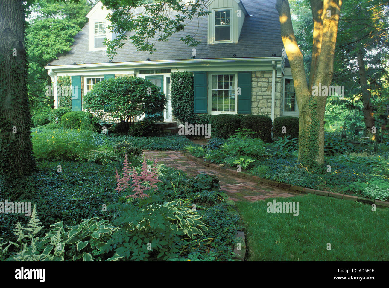 Cape Cod style stone house and brick pathway surrounded by trees in a  shaded garden Midwest USA Stock Photo - Alamy
