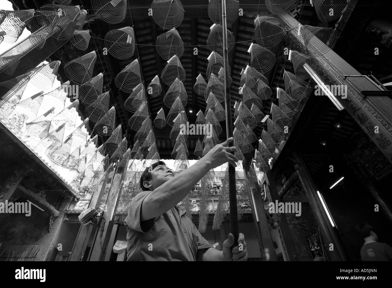 Southeast Asia Vietnam Ho Chi Minh City Worker lifts incense coils burning clouds of smoke inside Thien Hau Pagoda Stock Photo