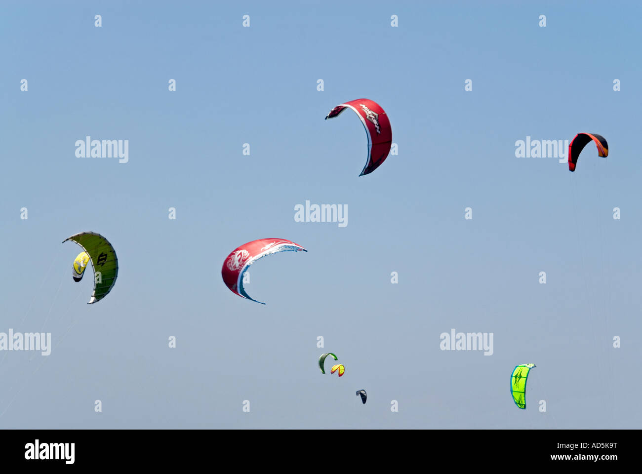 Horizontal view of a brightly coloured canopies from kitesurfers, overhead against a bright blue sky . Stock Photo