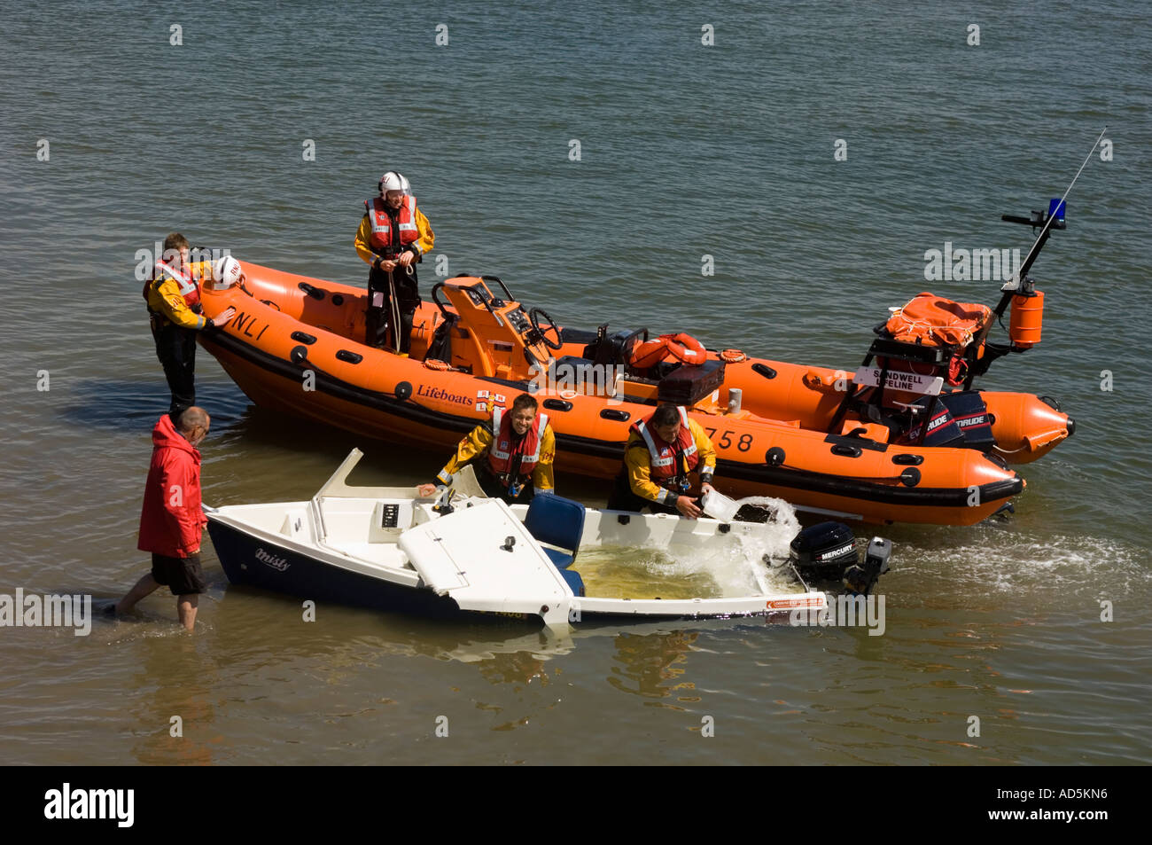 RNLI inshore rescue team bailing out a small boat in shallow water at Aberdyfi Aberdovey Gwynedd Snowdonia North Wales Stock Photo