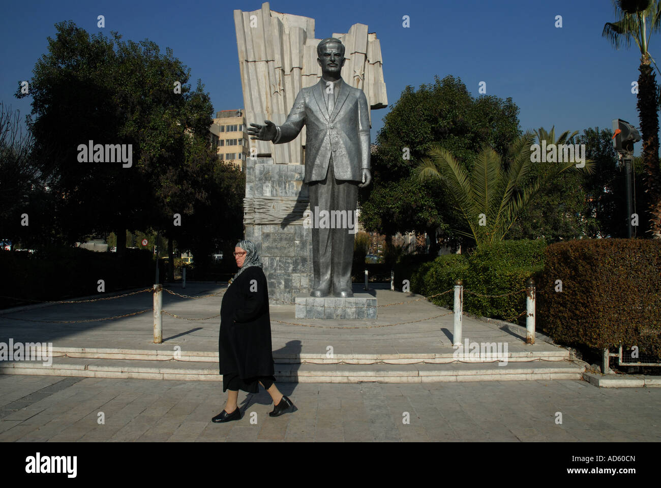 Damscus Syria Older woman walking past statue of ex President Hafez al Assad Stock Photo