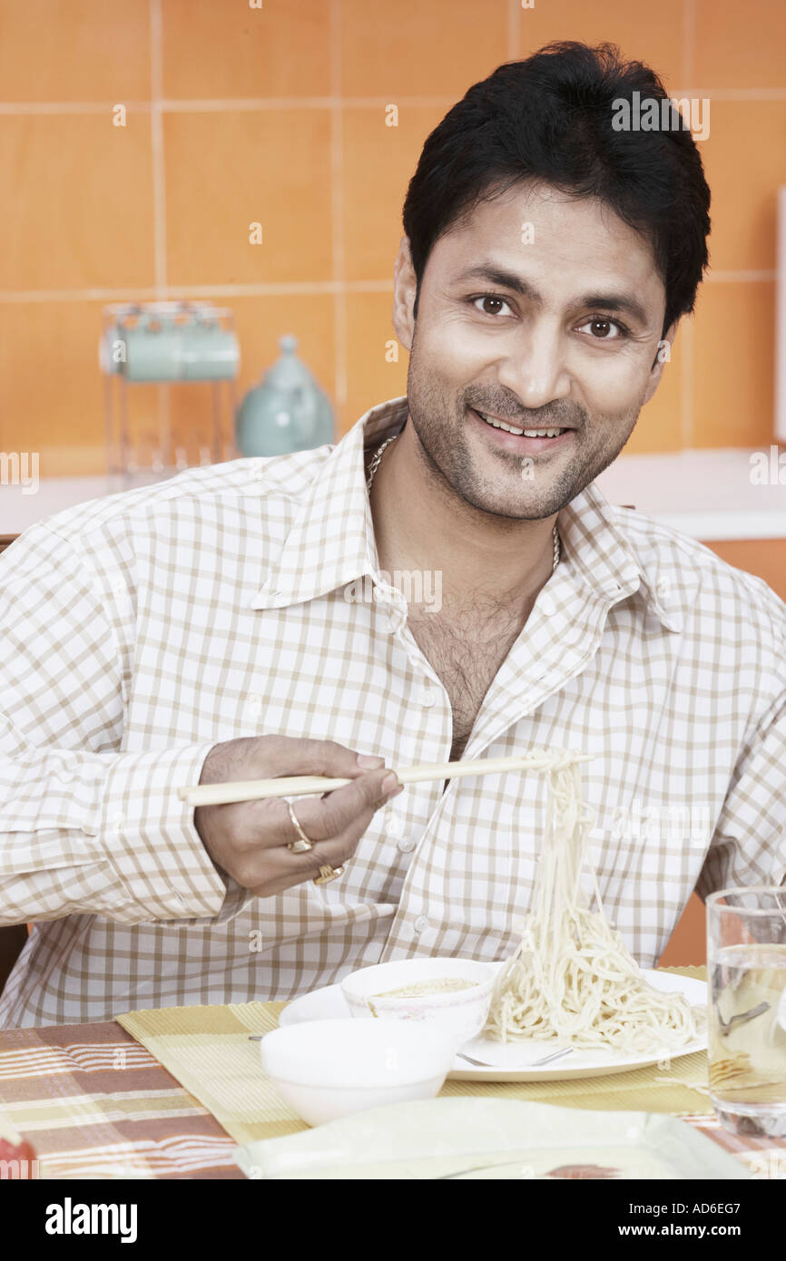 Portrait of a mid adult man holding noodles with a pair of chopsticks Stock Photo