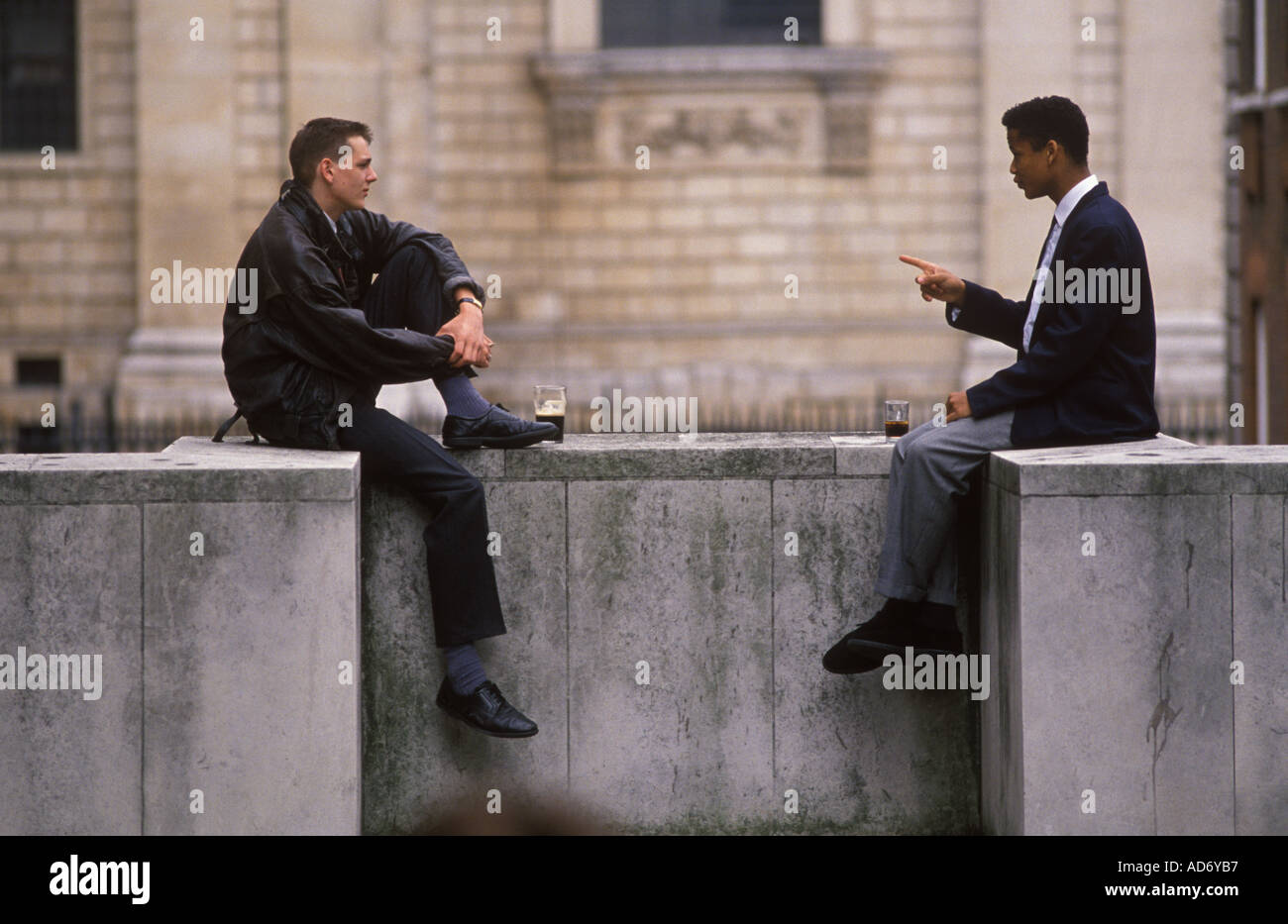 Two young men sitting on wall in a discussion over a pint of beer Finger pointing London   HOMER SYKES Stock Photo