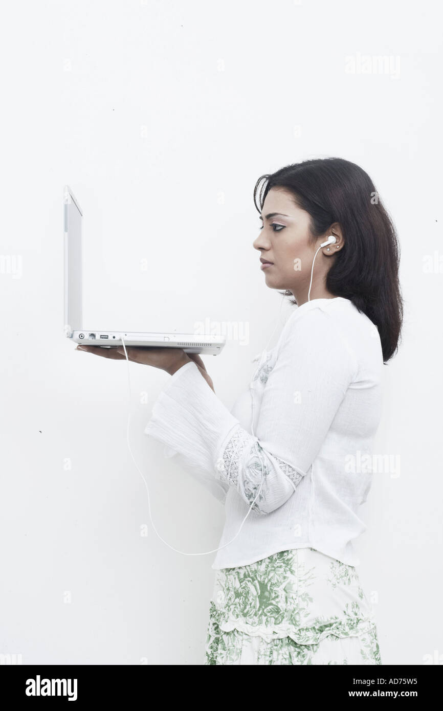 Side profile of a young woman wearing headphones holding a laptop Stock Photo