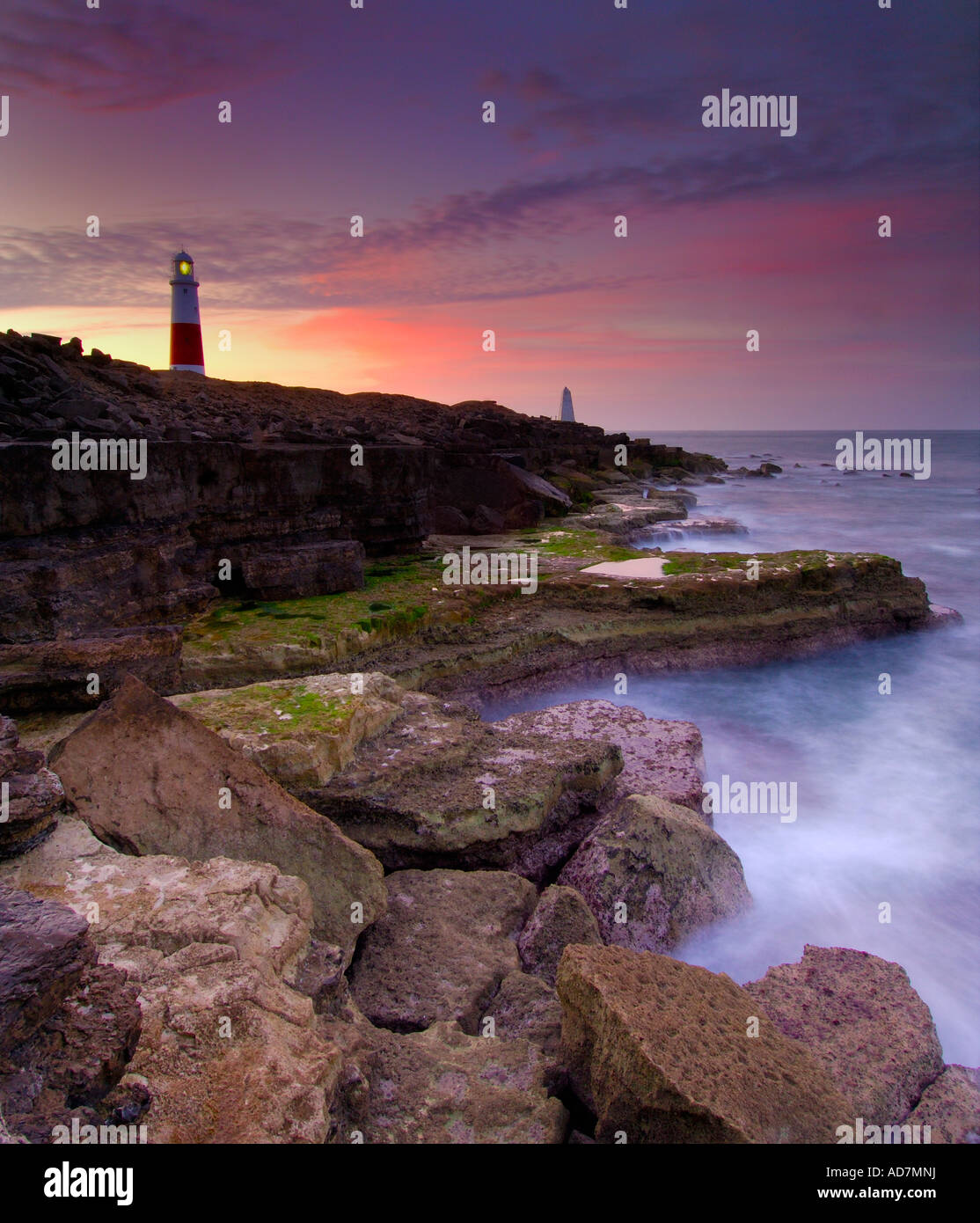 Portland Bill lighthouse just before dawn with the sea at low tide swirling around the treacherous headland rocks Stock Photo